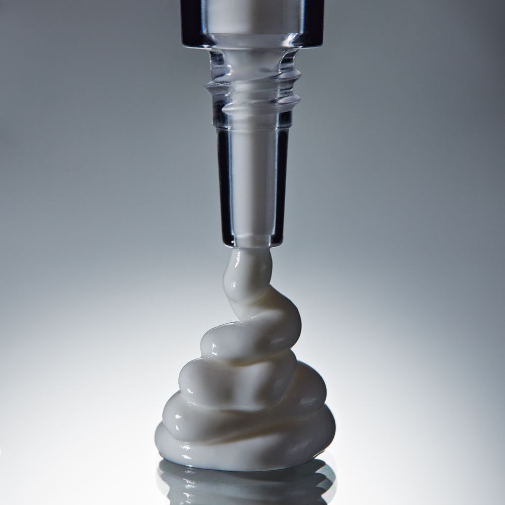 White cream being squeezed from a black and clear bottle onto a gray background