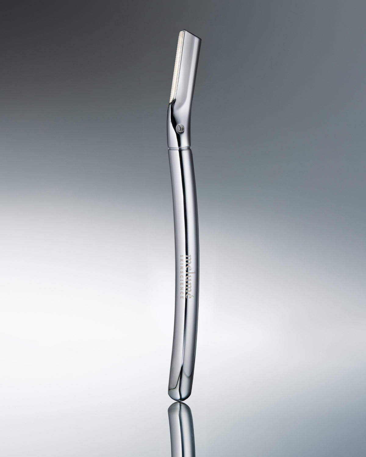 A polished stainless steel electric razor standing vertically on a reflective gray surface against a gradient gray background.