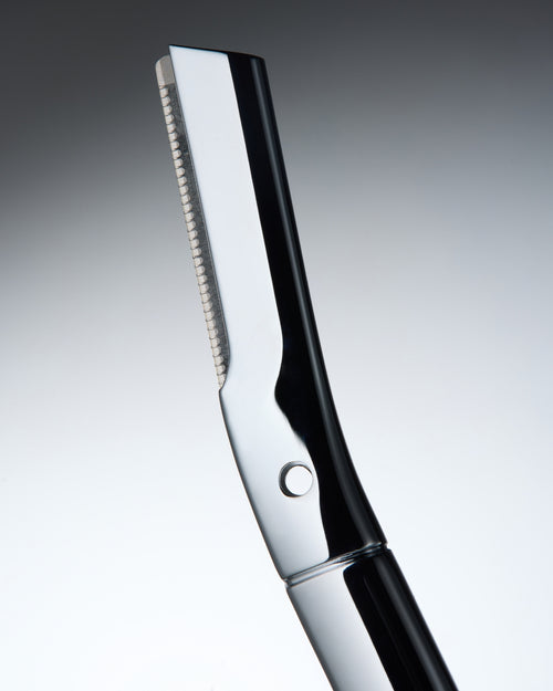 Carica immagine 2 in visualizzazione galleria. A close-up studio shot of a professional eyebrow razor with a polished silver metallic blade and a glossy black handle, set against a smooth gray gradient background.